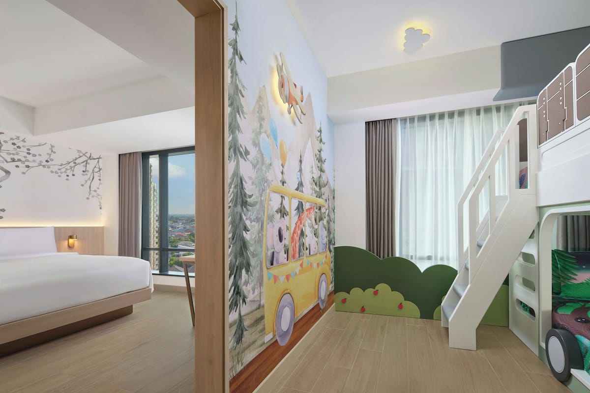 Une chambre d’hôtel avec un lit, une fresque représentant un autobus, un escalier et une vue sur la ville.