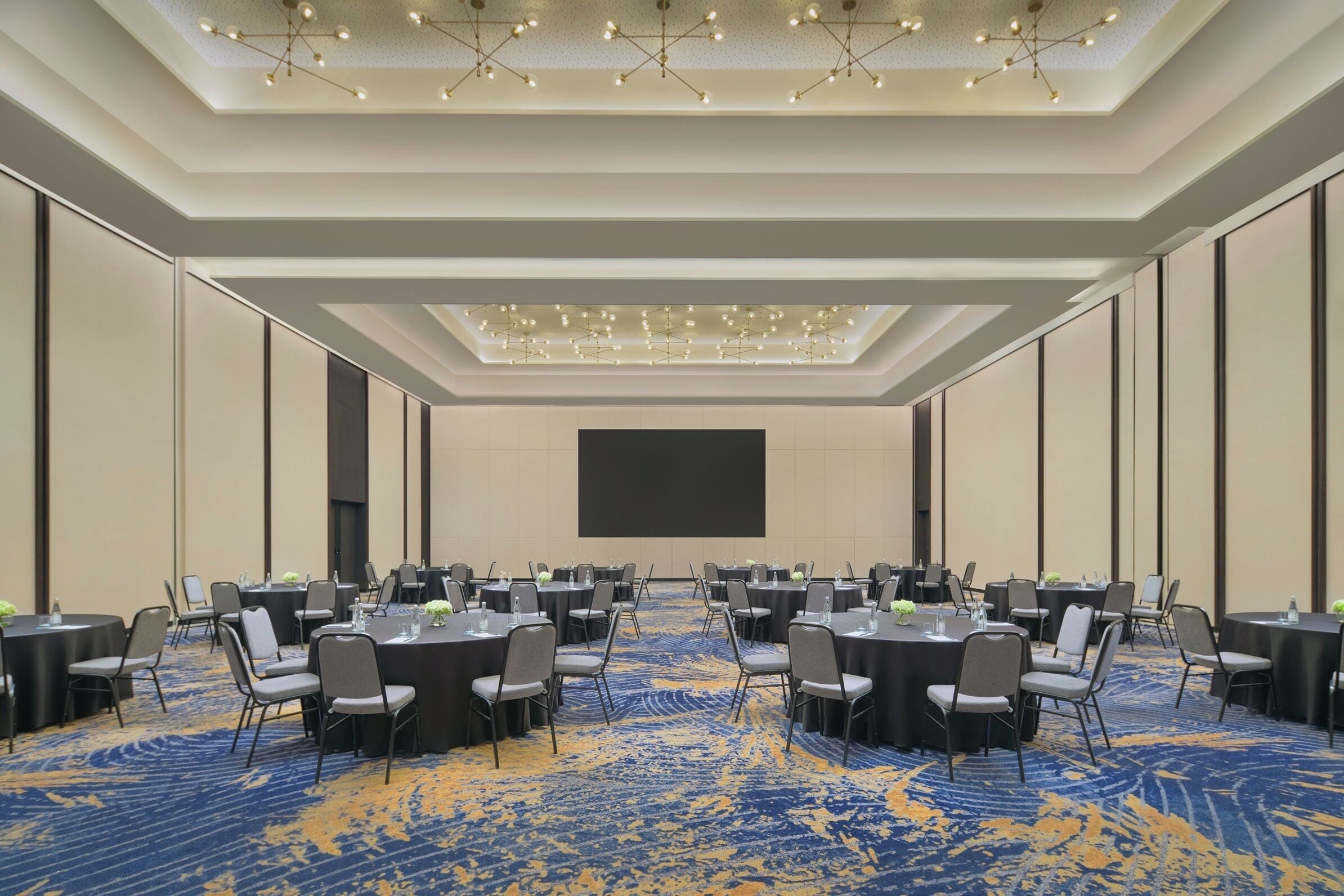 Un salón de conferencias con mesas redondas, sillas y una pantalla grande.