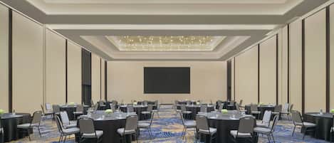 Un salón de conferencias con mesas redondas, sillas y una pantalla grande.