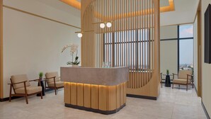 A reception area with a curved reception desk, wooden slats, and two chairs. - Fairfield By Marriott Bekasi (Bekasi)
