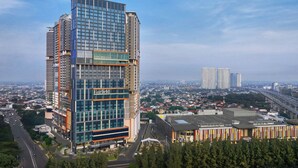 Un edificio de gran altura con fachada de vidrio moderno, con la leyenda "Fairfield", rodeado por un paisaje urbano con otros edificios altos y una autopista.