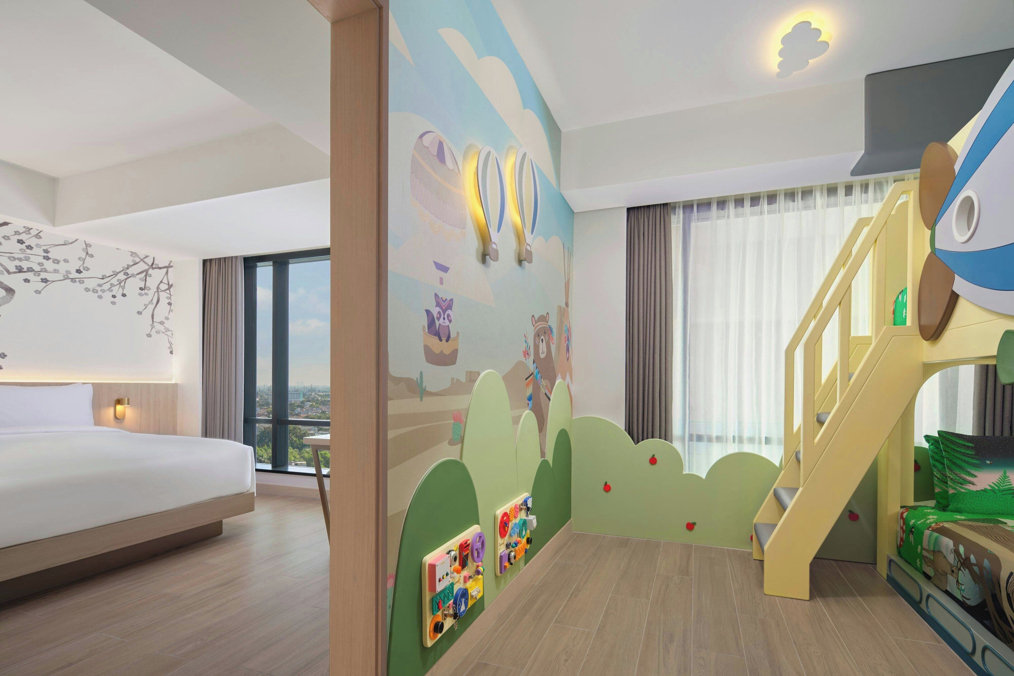 Une chambre d’hôtel avec un grand lit, un espace de jeux pour enfants et une vue sur la ville.