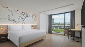 Quarto de hotel moderno com uma cama grande, uma escrivaninha e vista para a cidade.