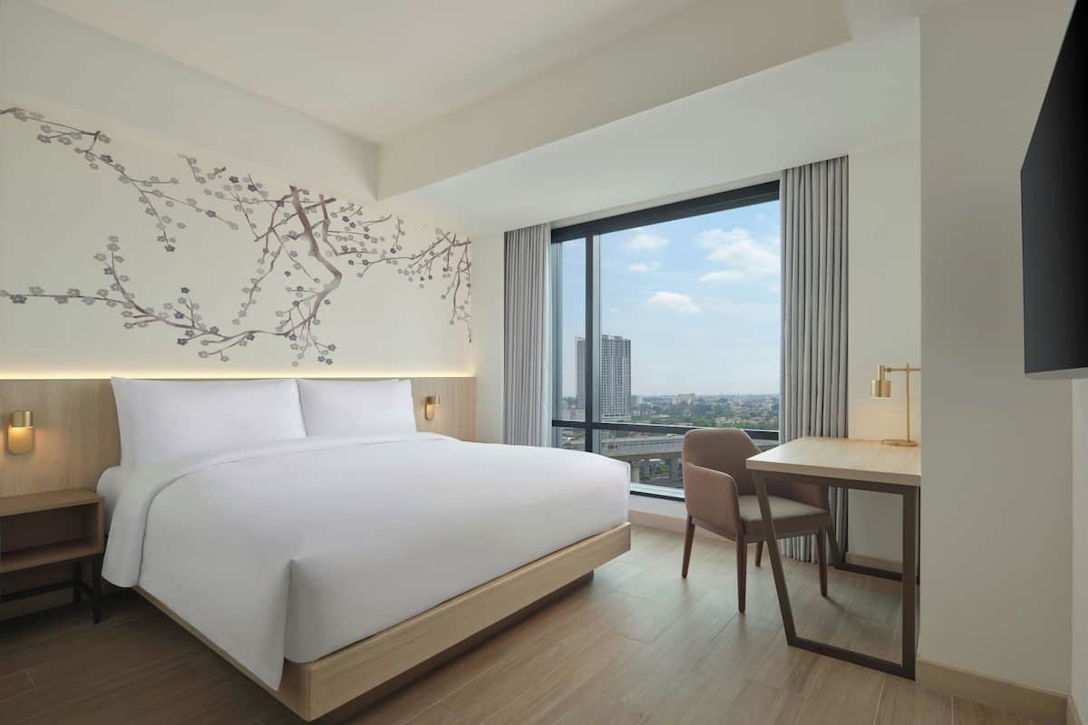 Une chambre d’hôtel moderne, dotée d’un grand lit, d’un bureau et offrant une vue sur la ville grâce à une grande fenêtre.