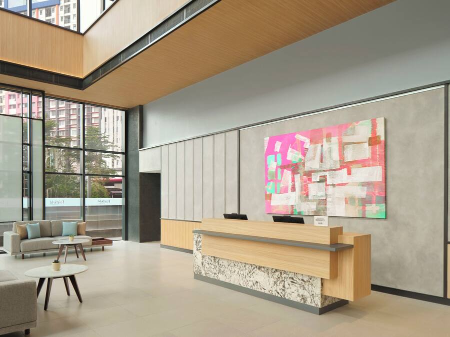 Un área de recepción moderna con un mostrador de madera, un cuadro abstracto colorido en la pared y una zona de estar con sofá y mesa de centro.