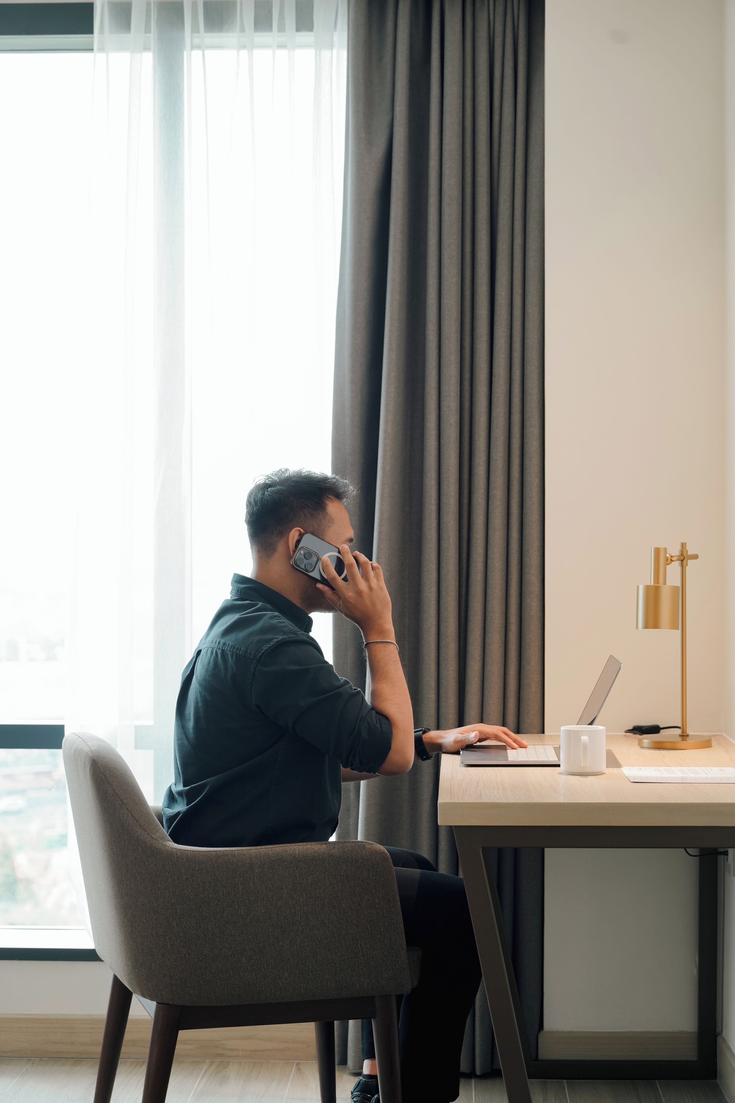 Iemand zit aan een bureau met een laptop, een smartphone en een kopje.