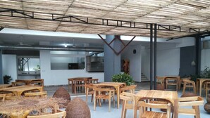 A spacious indoor dining area with wooden tables and chairs, a high ceiling with a bamboo-like structure, and a kitchen area in the background. - Hotel Ayapel Paraiso (Ayapel)