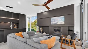 A modern living room with a grey sectional sofa, a wooden rocking chair, and a fireplace.