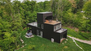 A modern, multi-level house with a flat roof, large windows, and a deck.