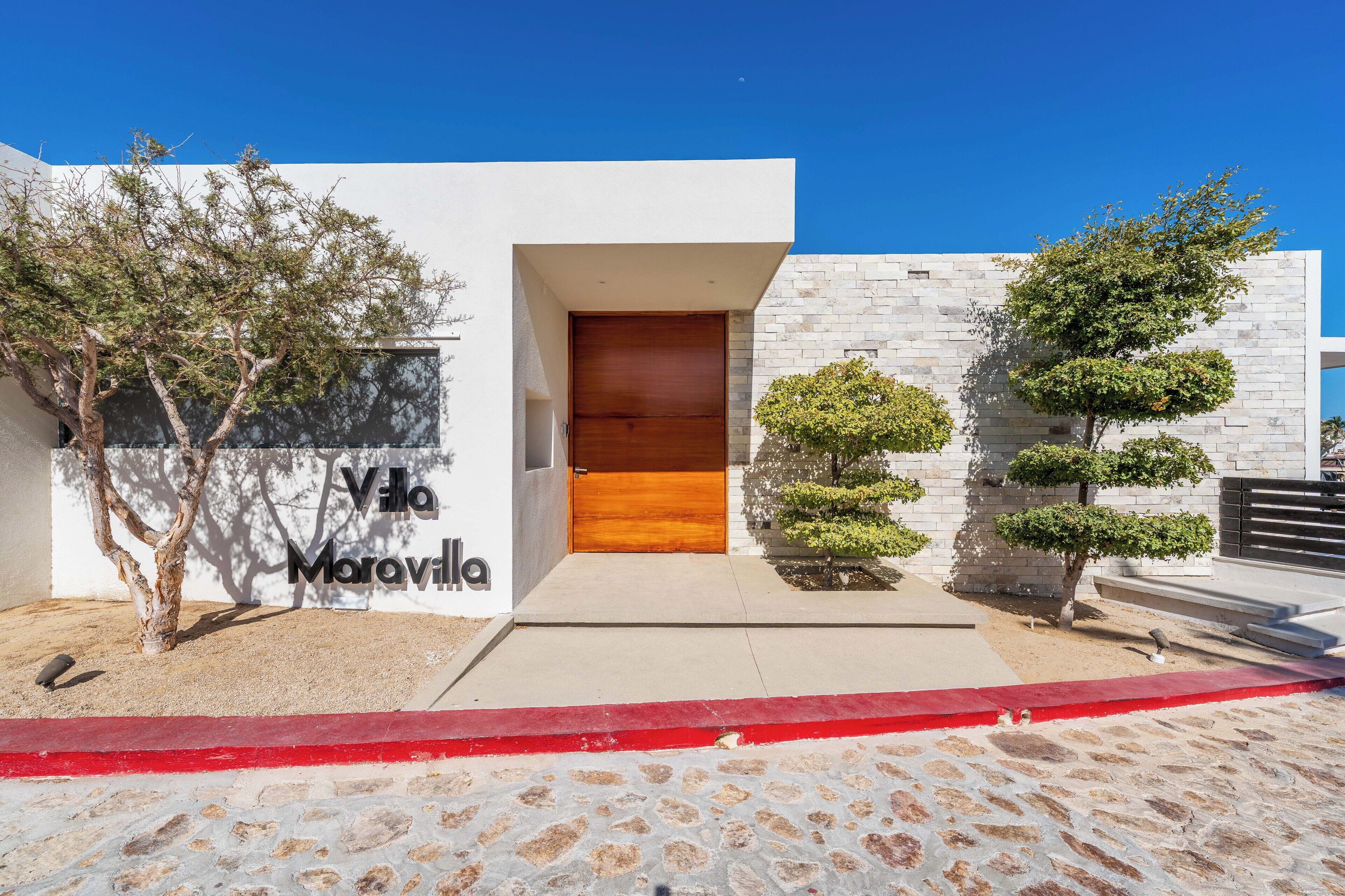 A modern villa with a wooden door, white walls, and a stone pathway.