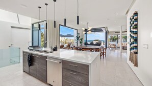 A modern kitchen with a central island, pendant lighting, and a view of the outdoors. - Villa Maravilla at Pedregal (Cabo San Lucas)