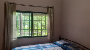 A bedroom with a bed, a window with curtains, and a view of greenery outside.