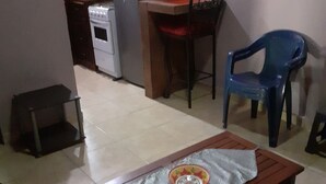 A compact living space with a kitchenette, a dining table with a bowl, and a blue chair.