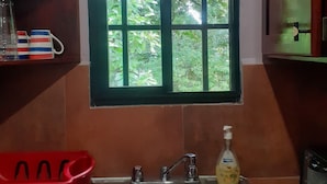 A kitchen with a stainless steel sink, a window with a view of greenery, and a shelf with kitchenware.