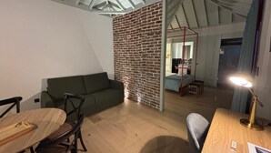 A modern interior with a brick partition, a green sofa, wooden furniture, and a visible kitchen area.