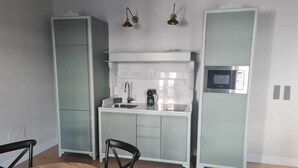 A compact kitchen with a sink, a microwave, and a coffee maker. There are two chairs and a round table.