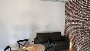 A room with a round wooden table and four chairs, a dark green sofa, and a brick-patterned wall.