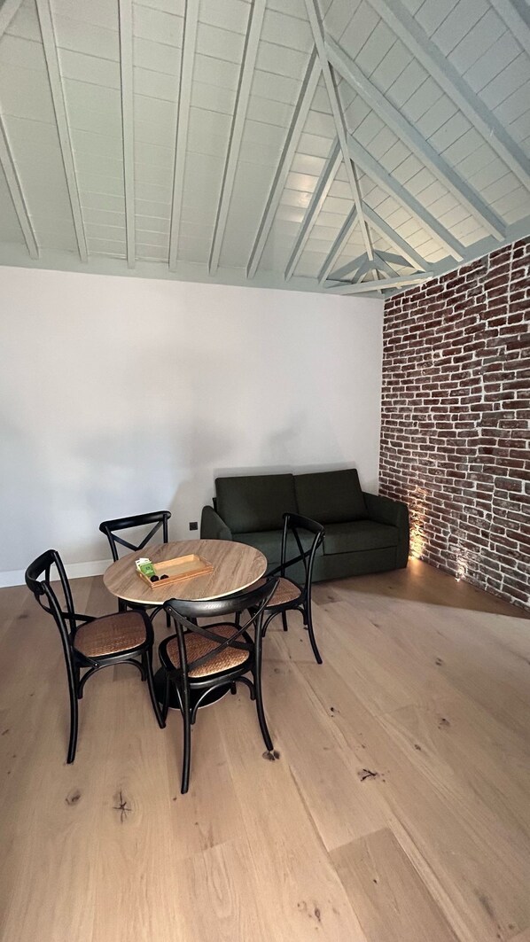 A room with a round wooden table and four chairs, a dark green sofa, and a brick-patterned wall.