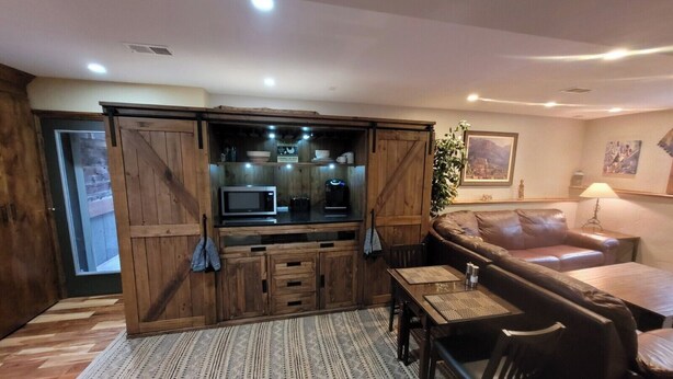 A cozy living room with a wooden entertainment unit, a leather sofa, and a dining area. - Exclusive 2 Bedroom Garden Level Apartment in Lovely Littleton Colorado! (Littleton)