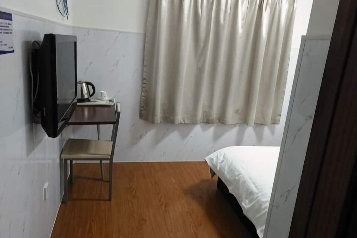 A room with a bed, a desk with a television, a chair, and a window with curtains.