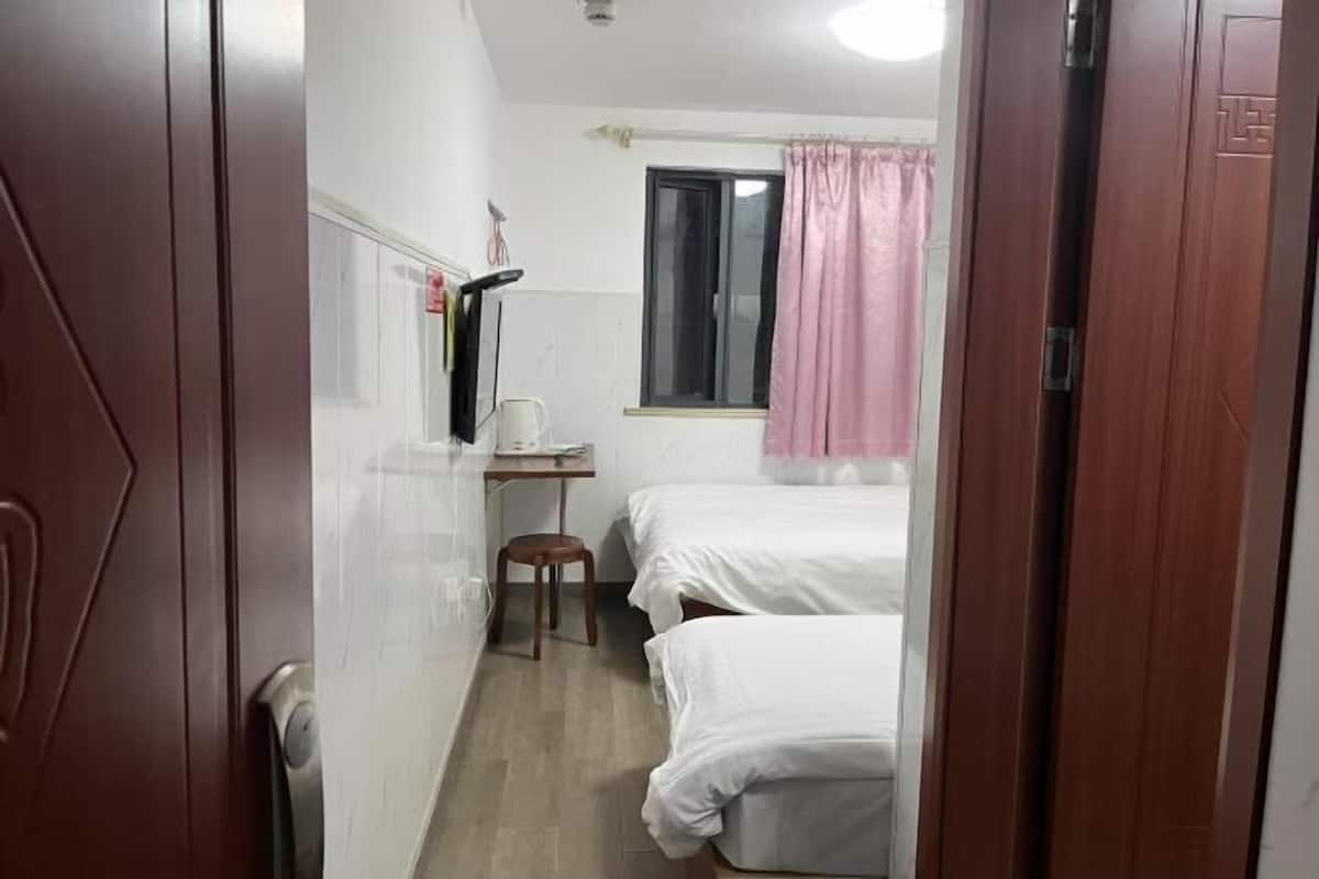 A narrow room with two beds, a desk, and a window with a curtain.