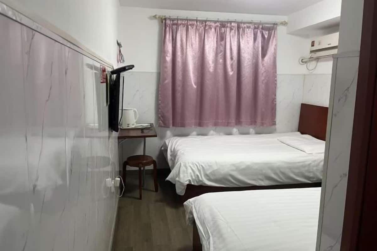 A bedroom with two beds, a desk, a chair, and a window with curtains.