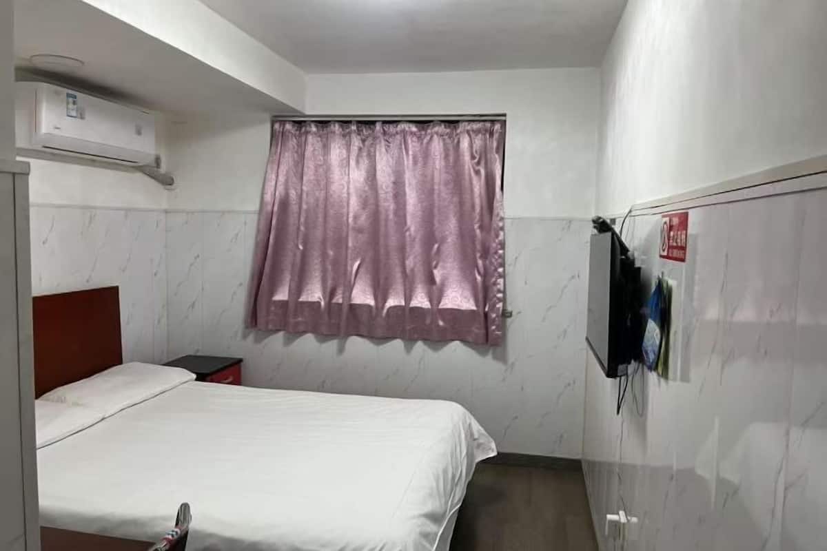 A bedroom with a bed, a window with a curtain, a wardrobe, and an air conditioning unit.