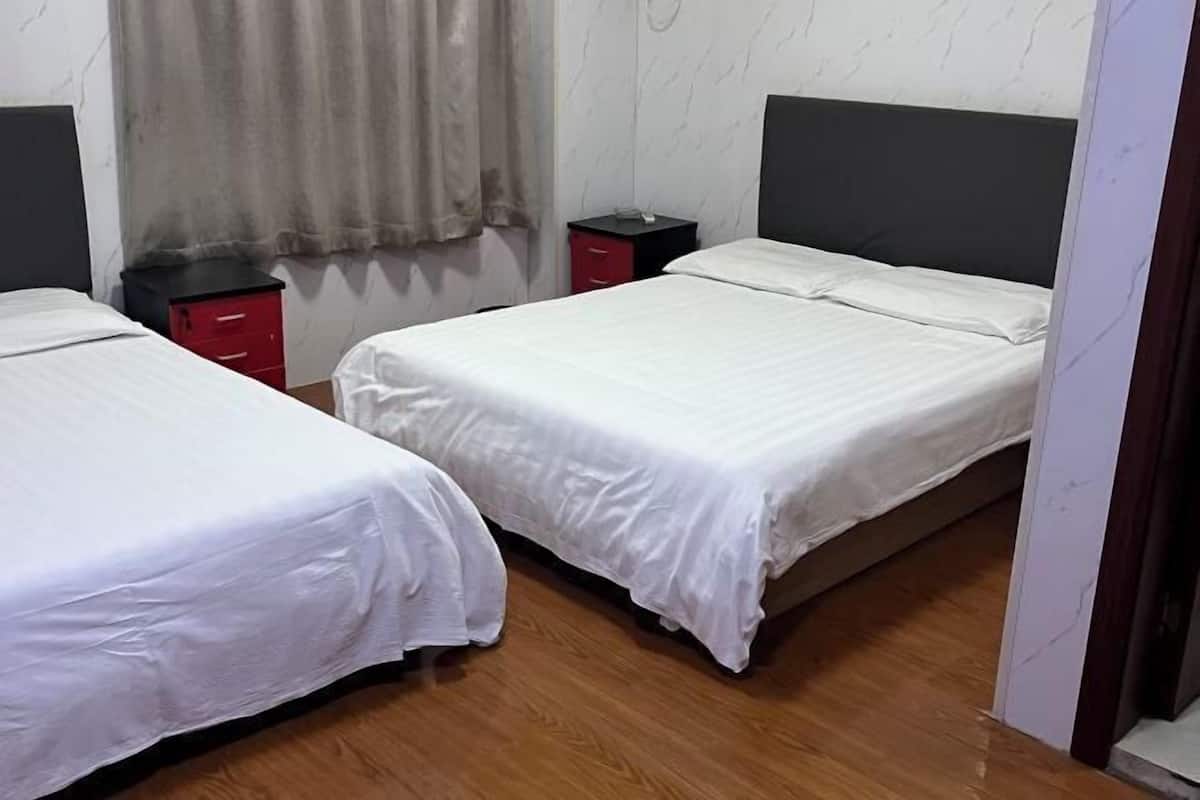A bedroom with two single beds, wooden flooring, a dark headboard, and a red nightstand.