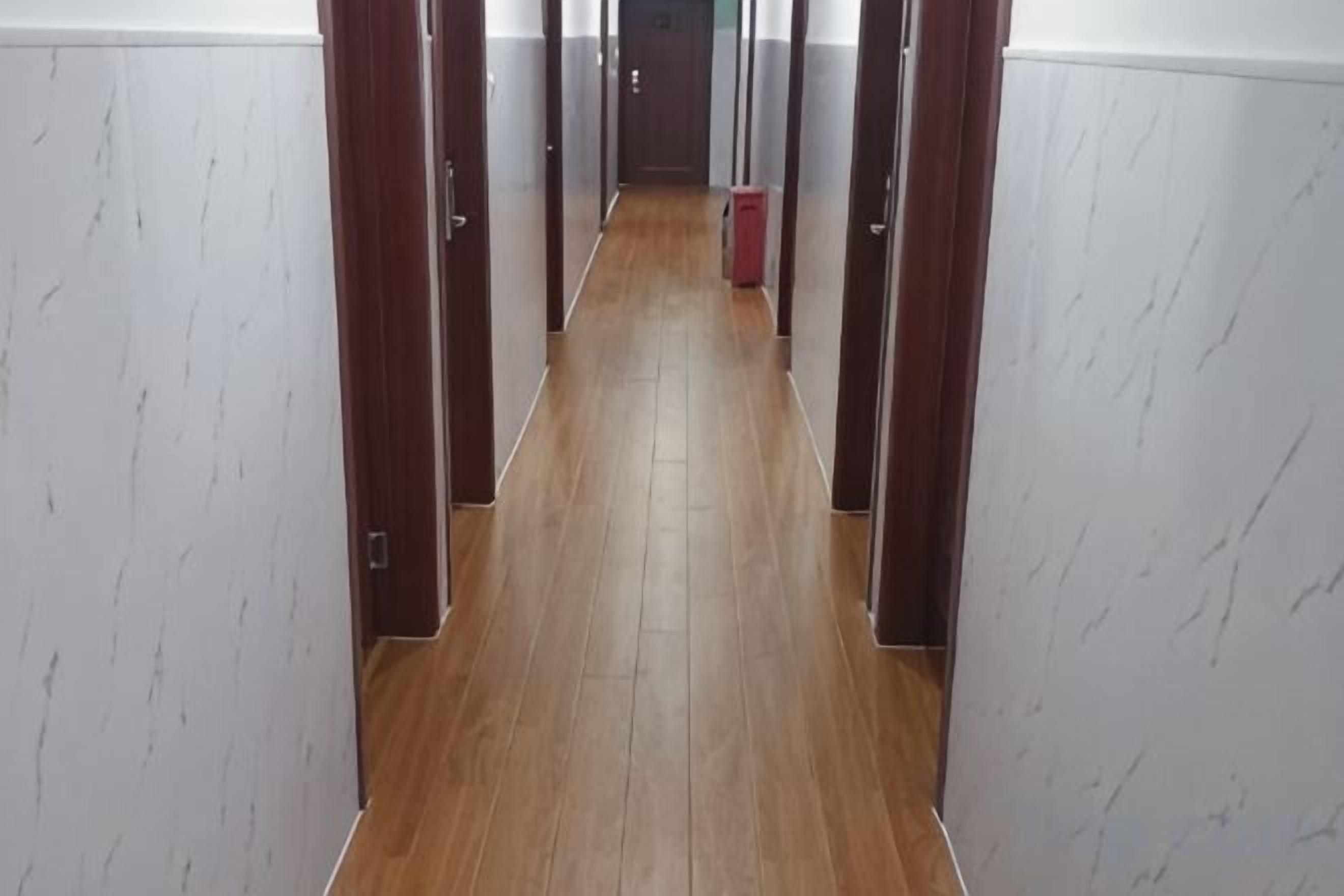 A narrow hallway with wooden flooring and white walls with a subtle pattern.