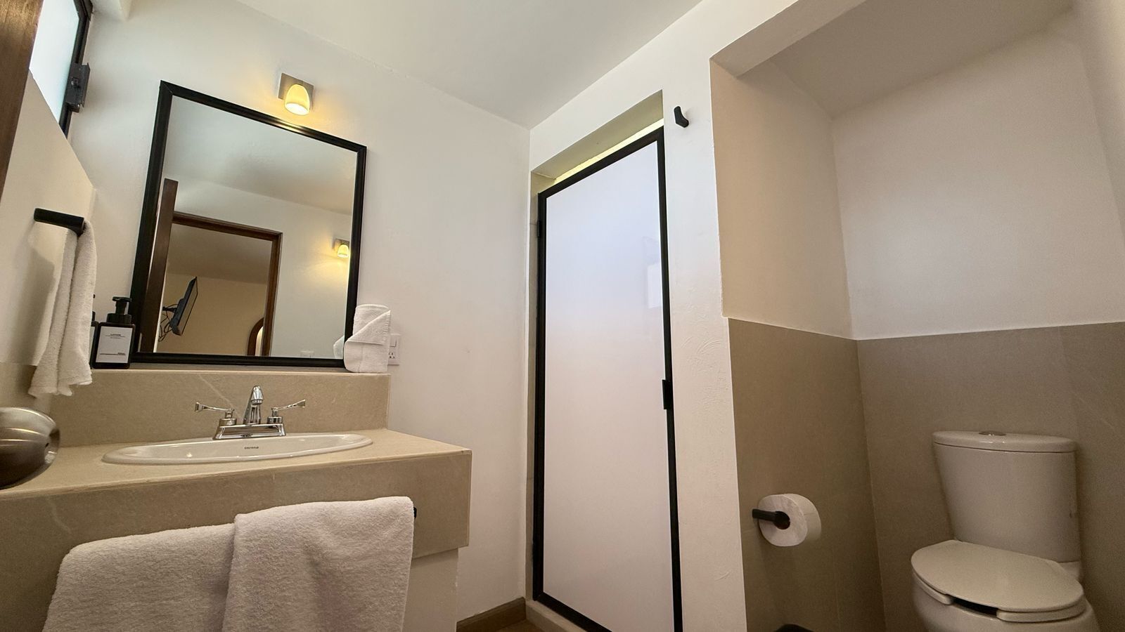 A bathroom with a sink, mirror, towel, toilet, and a door.