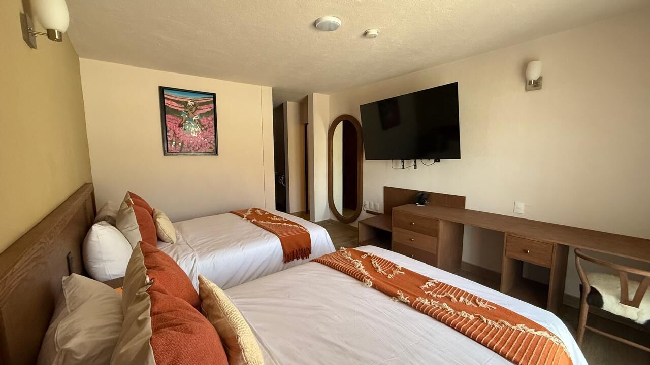 A hotel room with two beds, a desk, a chair, a TV, and a mirror.