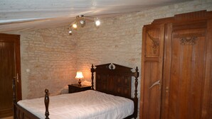 Een slaapkamer met een houten baldakijnbed, een stenen muur en een houten garderobe.