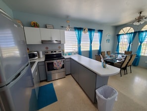 Compact kitchen with refrigerator, microwave, stove, and oven, featuring a dining area with table and chairs.
