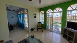 A living room with a glass coffee table, a ceiling fan, and large windows with decorative metal grilles. - Beautiful home with 2 bedrooms 2 minutes from the beach. (Rincon)