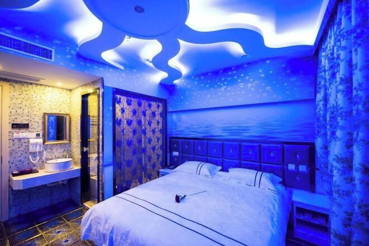 A bedroom with a bed, a nightstand, a wall-mounted TV, and a bathroom with a sink and mirror.