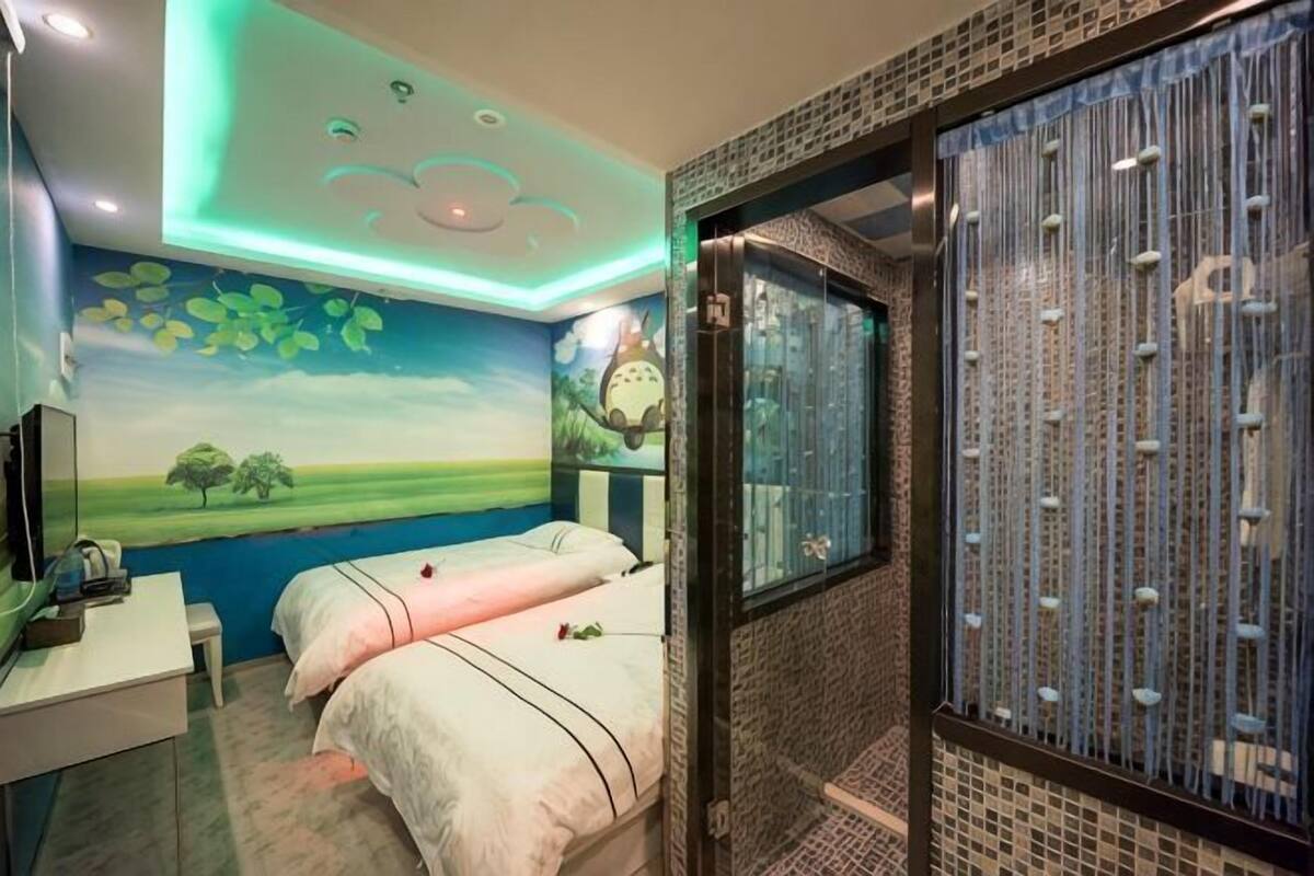 A bedroom with a bed, a desk, a mirror, a window, and a bathroom with a shower.