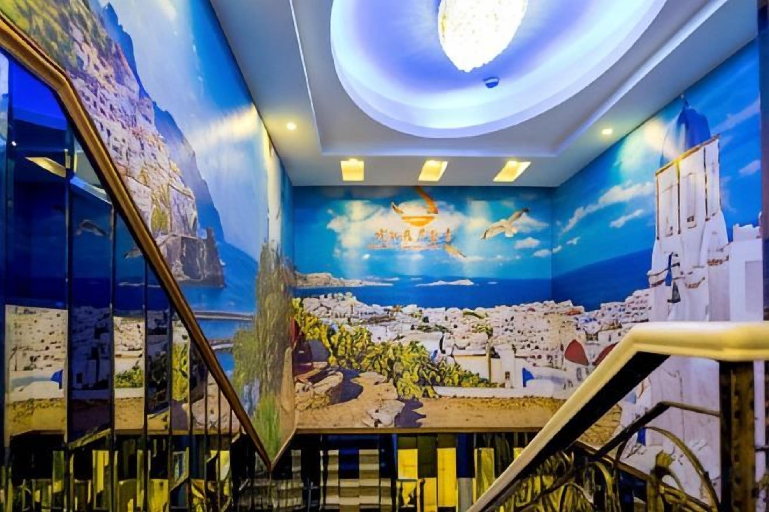 A room with a mural of a coastal town, a staircase, and a circular light fixture on the ceiling.