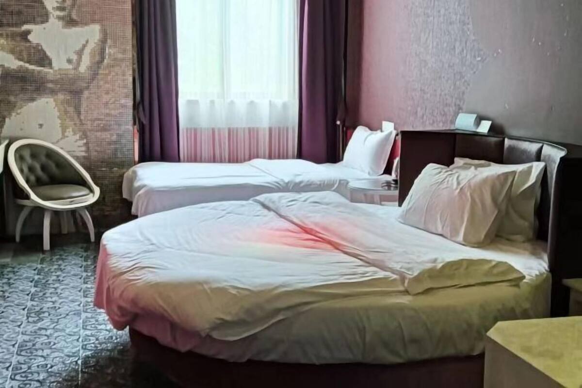 A hotel room with two beds, a chair, a nightstand, and a wall with a decorative pattern.