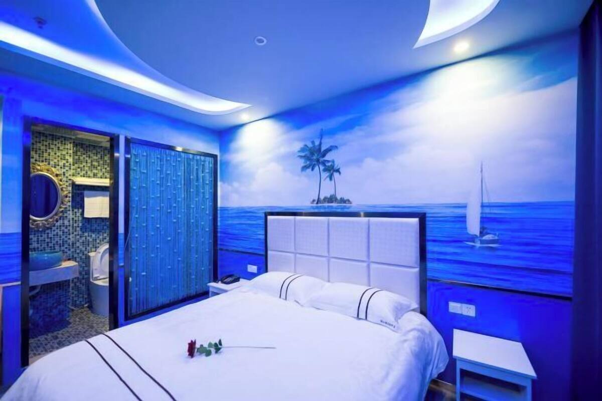 A modern bedroom with a large bed, a bathroom with a tiled wall, and a mural of a beach scene.