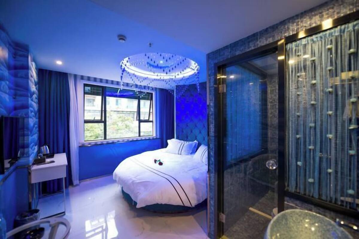 A bedroom with a bed, a desk, a window, and a glass shower enclosure.