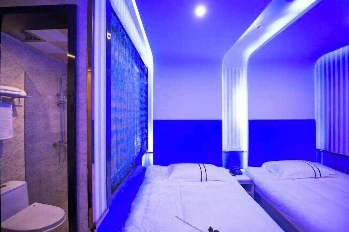 A hotel room with a shower, two beds, a nightstand, and a painting on the wall.