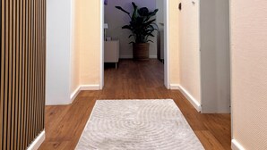 Un pasillo con suelo de madera, alfombra blanca y una planta en maceta.