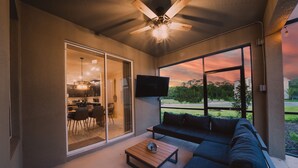 Ein geräumiger Balkon mit Deckenventilator, einem dunkelgrauen Sofa, einem kleinen Holztisch und einem an der Wand befestigten Fernseher.