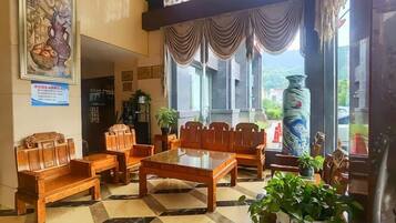 A lobby with a checkered floor, wooden furniture, a large vase, and a painting on the wall.