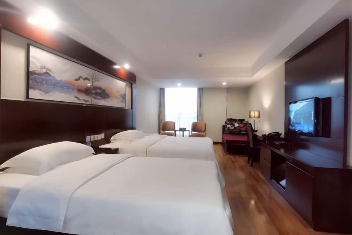 Une chambre d’hôtel avec deux lits, un bureau avec une chaise, une télévision et un tableau au mur.