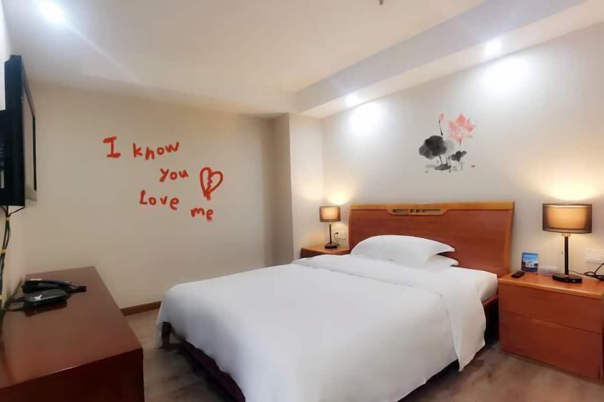 Une chambre d’hôtel comprenant un lit, des tables de chevet, un bureau, un mur décoré d’un motif en forme de cœur et une œuvre d’art murale.