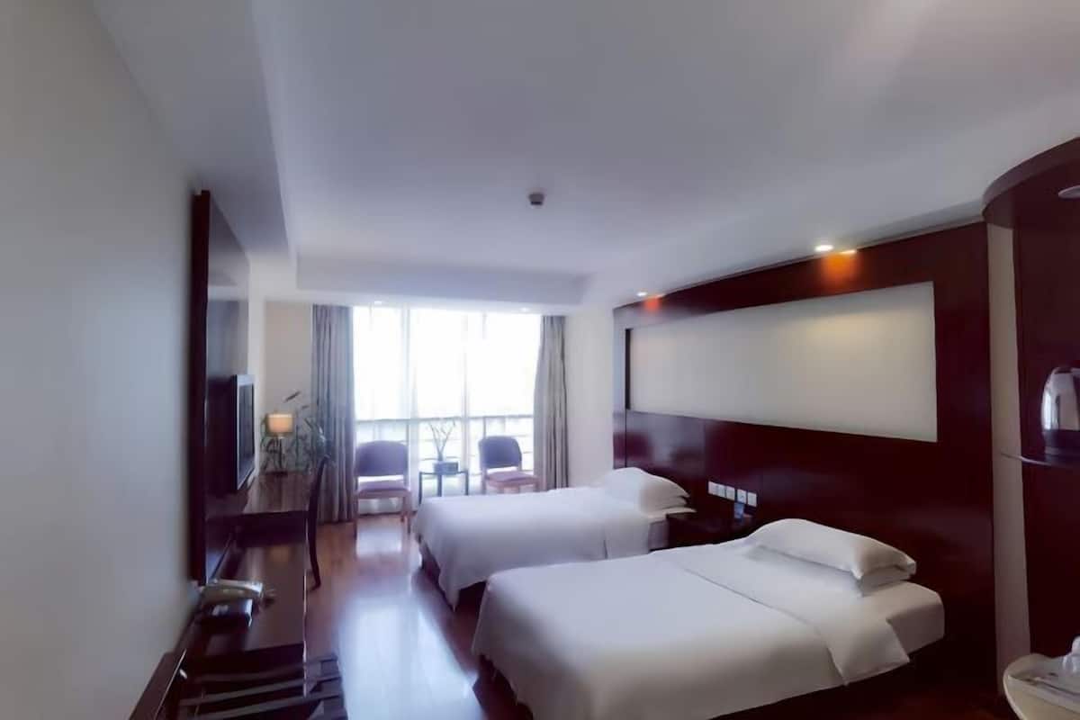 Une chambre d’hôtel avec deux lits, un bureau, une chaise, une télévision et une grande fenêtre.