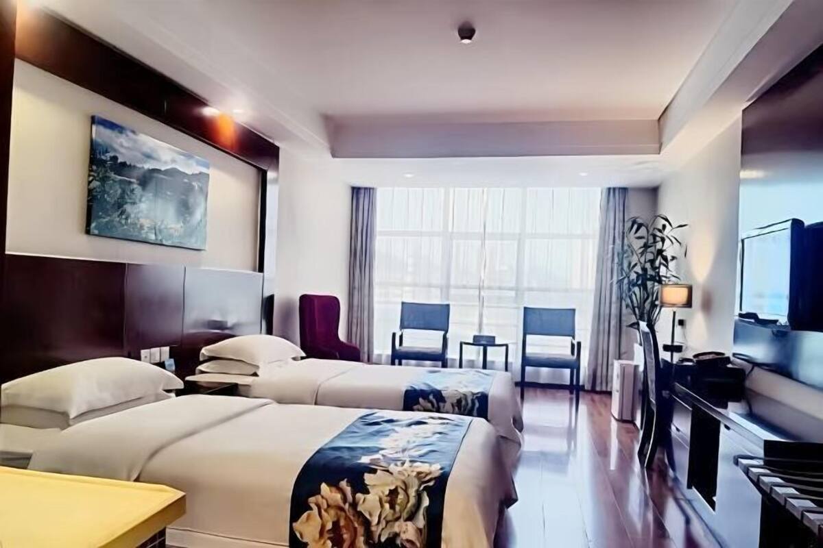 Une chambre d’hôtel avec deux lits, une grande fenêtre, un téléviseur à écran plat et un bureau avec une chaise.