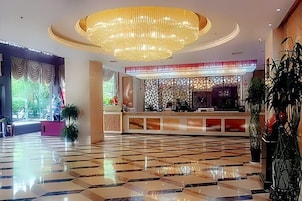 Un hall de hotel con mostrador de recepción, una araña y suelo de baldosas.