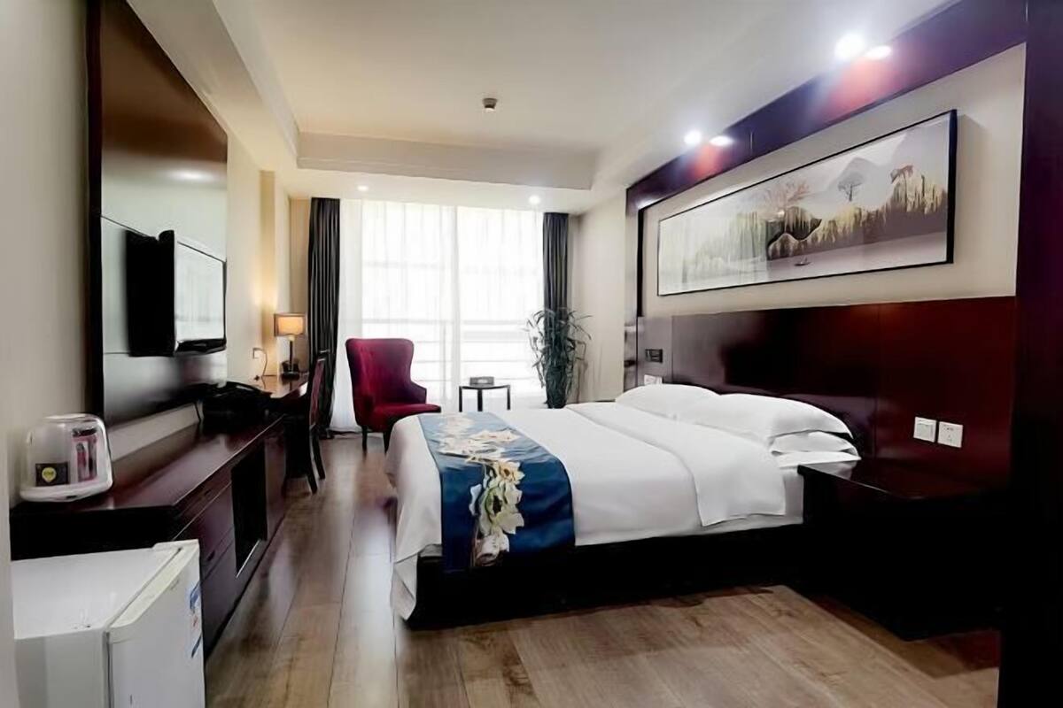 Une chambre d’hôtel avec un lit, un bureau doté d’une lampe, une chaise, un téléviseur et un tableau au mur.